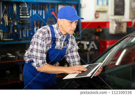 Mechanic man with laptop making car diagnostics at service 112100336