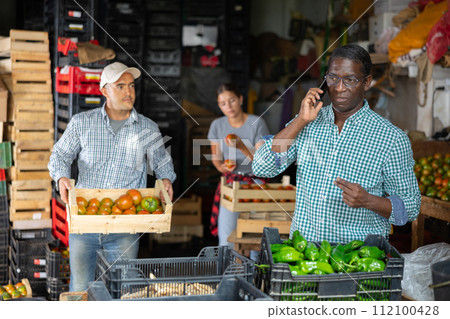 African american farmer using smartphone while working in vegetables sorting warehouse 112100428
