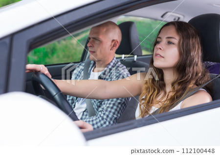 Confident young woman driving car with man in passenger seat Confident young woman driving car with man in passenger seat 112100448