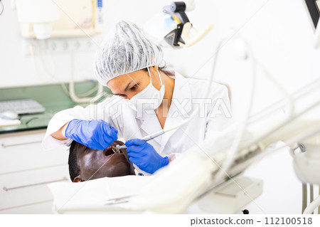 Focused female dentist with patient during teeth treatment in dental office Focused female dentist with patient during teeth treatment in dental office 112100518