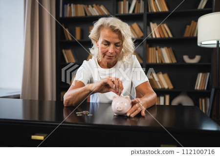 Saving money investment for future. Senior adult mature woman putting money coin in piggy bank. Old grandmother counting saving money planning retirement budget. Investment banking concept Saving money investment for future. Senior adult mature woman putting money coin in piggy bank. Old grandmother counting saving money planning retirement budget. Investment banking concept 112100716