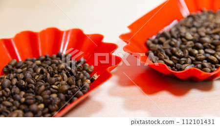 Roasted arabica coffee grains are in red plastic trays, close-up 112101431