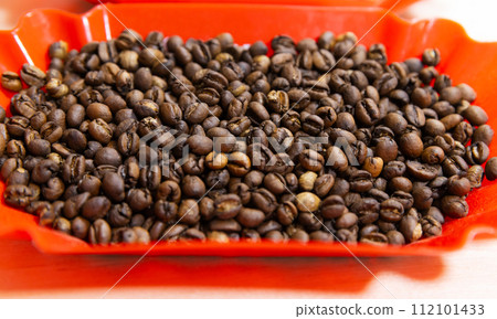 Roasted selective arabica coffee beans are in red plastic tray, close-up 112101433