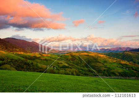 carpathian countryside scenery with grassy meadows and forested hills in evening light. mountainous rural landscape of transcarpathia, ukraine in spring 112101613