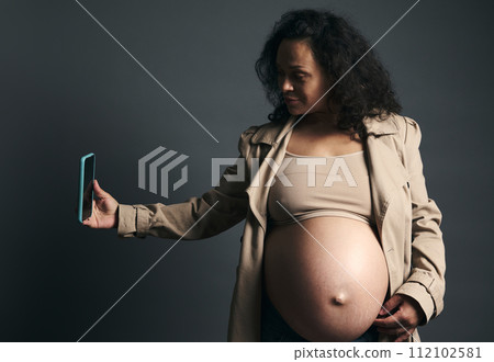 Attractive beautiful young gravid female, expectant mother photographing her tummy in third trimester of happy pregnancy Attractive beautiful young gravid female, expectant mother photographing her tummy in third trimester of happy pregnancy 112102581