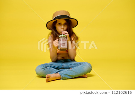 Adorable little girl 6 years old in summer clothes and straw hat, with delicious refreshing drink, isolated on yellow Adorable little girl 6 years old in summer clothes and straw hat, with delicious refreshing drink, isolated on yellow 112102616