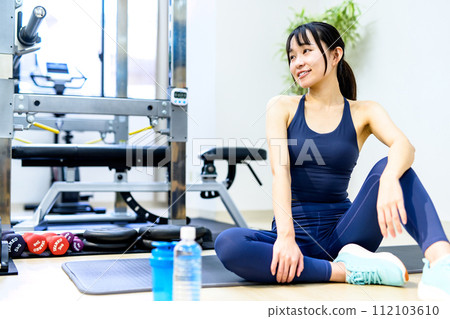 A young smiling woman training her body at a personal gym, taking a break, background material, muscle training girl, indoor color, clear 112103610