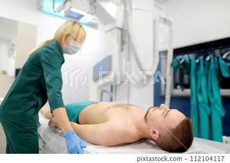 Female radiologist going to made x-ray shot of young male patient in x-ray room in modern clinic 112104117