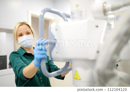 Female technician adjusts X-Ray machine. Female radiologist is going to take an Xray of patient in X-ray room of modern clinic. Female technician adjusts X-Ray machine. Female radiologist is going to take an Xray of patient in X-ray room of modern clinic. 112104120