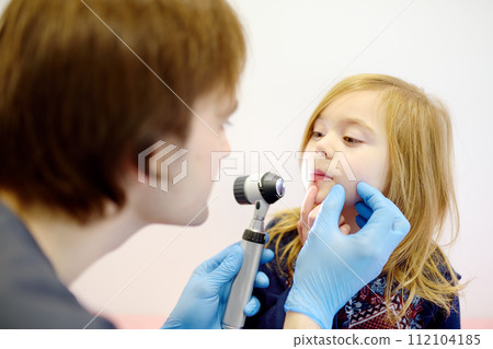Cute little girl during appointment of dermatologist in modern clinic. Male doctor looking a pimple on a lips of child. Treatment of herpes virus, streptococcus infection 112104185