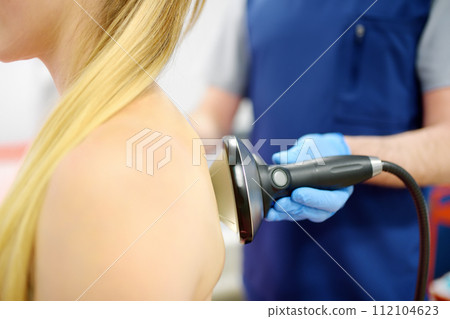 Close up of extracorporeal shockwave therapy in beauty salon. Physical therapy for neck, back and spine muscles with shock waves. Rehabilitation after injury. 112104623