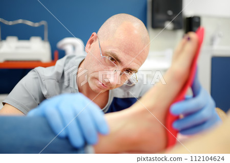 Orthopedic insoles. Fitting orthotic insoles. Flatfoot treatment. Podiatry clinic. Male orthopedist tries insole on patient's foot in clinic. Orthopedic insoles. Fitting orthotic insoles. Flatfoot treatment. Podiatry clinic. Male orthopedist tries insole on patient's foot in clinic. 112104624