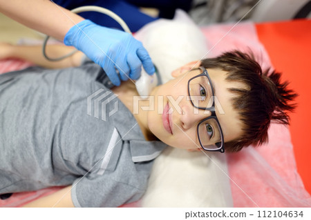 Doctor making ultrasound of the thyroid gland for boy using scanner machine. Female doc runs ultrasound sensor over patient neck for scanning of the thyroid gland and lymph nodes. 112104634