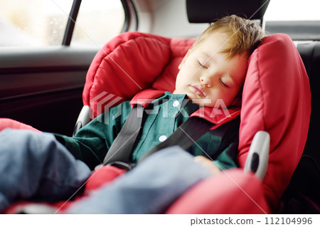 Cute toddler boy sleeping in car seat. Portrait of pretty little child during family road trip. Safety transportation of baby by car 112104996