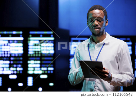 Focused admin using tablet to assess energy consumption across server rackmounts components. Employee making sure high tech data center mainframes temperature sensors are running smoothly Focused admin using tablet to assess energy consumption across server rackmounts components. Employee making sure high tech data center mainframes temperature sensors are running smoothly 112105542