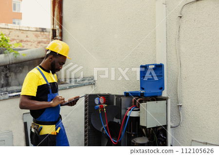 Competent mechanic doing air conditioner checkup, looking for leaks and other necessary repairs to prevent major breakdowns. Adept repairman troubleshooting condenser, writing findings on clipboard Competent mechanic doing air conditioner checkup, looking for leaks and other necessary repairs to prevent major breakdowns. Adept repairman troubleshooting condenser, writing findings on clipboard 112105626