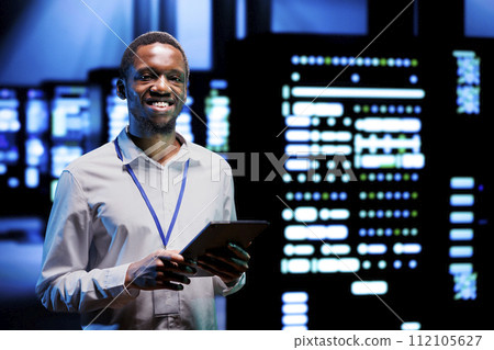 Portrait of smiling overseerer running data center devices diagnostic tests to determine and debug software problems. Happy serviceman using tablet to analyze critical systems, checking for crashes 112105627