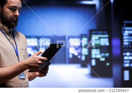 Repairman in server room between mainframes used for computationally intensive tasks such as scientific simulations or 3D rendering. Professional doing professional equipment inspection using tablet Repairman in server room between mainframes used for computationally intensive tasks such as scientific simulations or 3D rendering. Professional doing professional equipment inspection using tablet 112105657