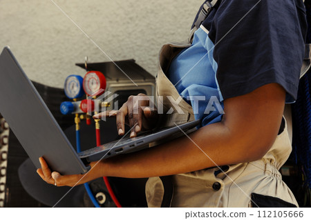 Specialist african american mechanic using laptop to look online for new capacitor after finding condenser malfuntioning internal component during business owner comissioned maintenance 112105666