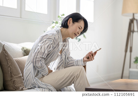 一名 50 歲出頭、腹痛的女性摀著小腹看著智慧型手機 112105691