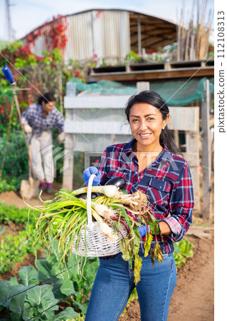 Smiling female gardener holding vegetables grown in home garden 112108313