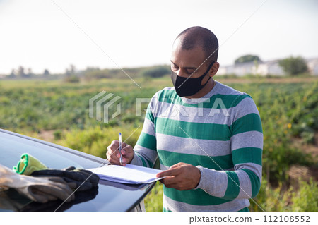 Farmer in protective mask signing papers near car Farmer in protective mask signing papers near car 112108552