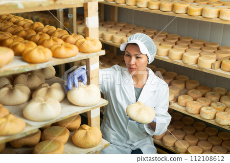 Woman cheesemaker checking aging process of cheese in maturing chamber 112108612