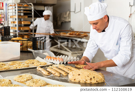 Male baker working with dough forming baguettes 112108619