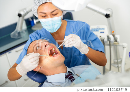 Qualified woman dentist in a protective mask treats a man patient 112108749