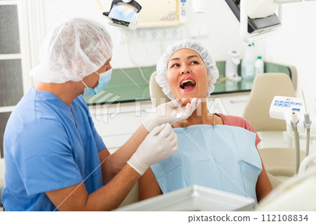 Qualified man dentist in a protective mask conducts an examines of a woman patient 112108834
