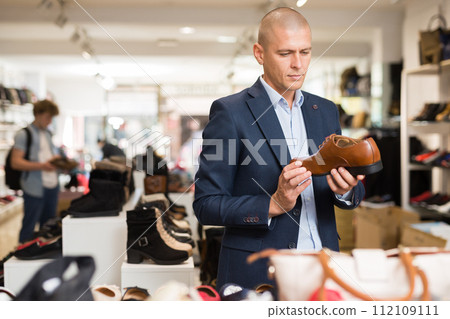 Focused man looking at brown leather dress shoe in store Focused man looking at brown leather dress shoe in store 112109111