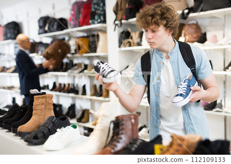 Satisfied teenager chooses sporty clothes and comfortable shoes from assortment in sports shop 112109133