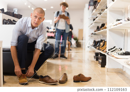 Handsome man trying on summer brown shoes in shoe store Handsome man trying on summer brown shoes in shoe store 112109163