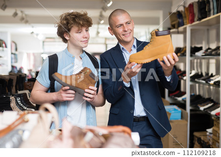 Father and son choose and buy fashionable brown winter boots in shoe store 112109218