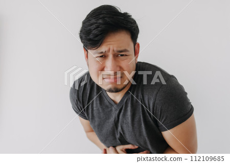 Asian man in black t-shirt feeling sick and stomach ache isolated on white. 112109685