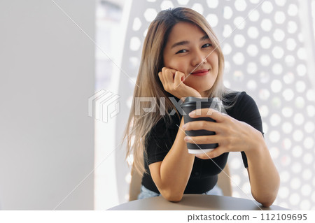 Happy woman in black t-shirt sipping hot coffee in white coffee shop. 112109695