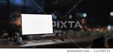 A white-screen PC computer mockup on a desk in a contemporary dark office at night. 112109725