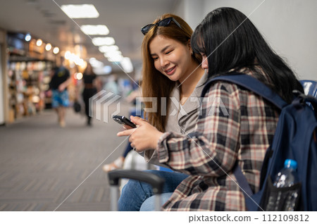 Two happy female friends are enjoy talking while waiting for their boarding time in the airport. Two happy female friends are enjoy talking while waiting for their boarding time in the airport. 112109812