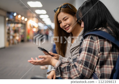 Two happy female friends are enjoy talking while waiting for their boarding time in the airport. Two happy female friends are enjoy talking while waiting for their boarding time in the airport. 112109813