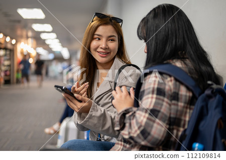 Two happy female friends are enjoy talking while waiting for their boarding time in the airport. 112109814