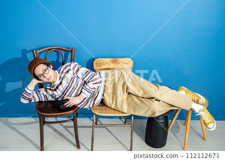 一個年輕人躺在藍色背景的椅子上 112112671