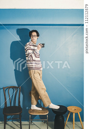 Young man working while standing on a chair with blue background Young man working while standing on a chair with blue background 112112879