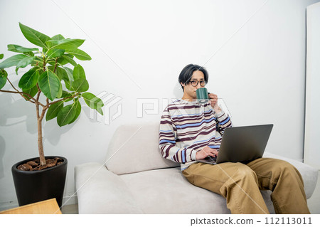 A man relaxing on a sofa drinking coffee and operating a computer 112113011