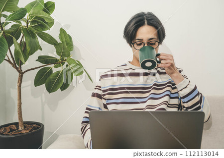 一個男人放鬆地坐在沙發上喝咖啡並操作電腦 一個男人放鬆地坐在沙發上喝咖啡並操作電腦 112113014