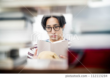 一個年輕人在大量書籍的包圍下讀書 112113284