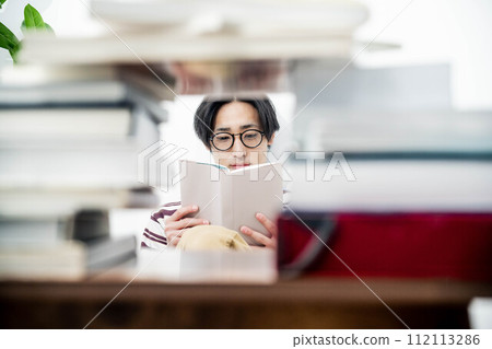 A young man reading while surrounded by a large number of books 112113286