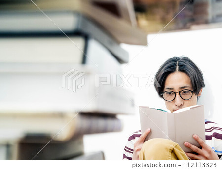 A young man reading while surrounded by a large number of books A young man reading while surrounded by a large number of books 112113323