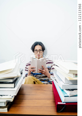 A young man reading while surrounded by a large number of books 112113368