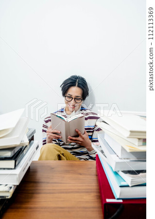 A young man reading while surrounded by a large number of books 112113369