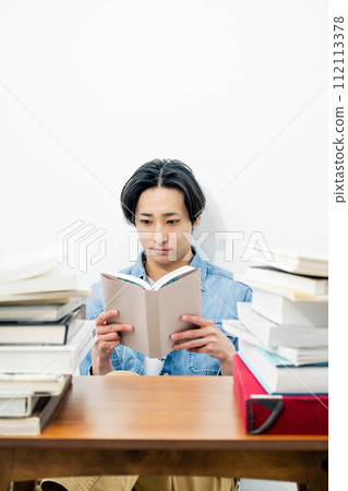 A young man reading while surrounded by a large number of books A young man reading while surrounded by a large number of books 112113378